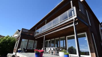 Uma casa moderna de dois andares, com janelas amplas, uma varanda e área de estar externa.