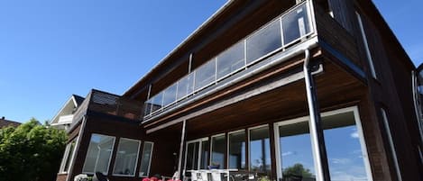 A modern two-story house with large windows, a balcony, and outdoor seating.