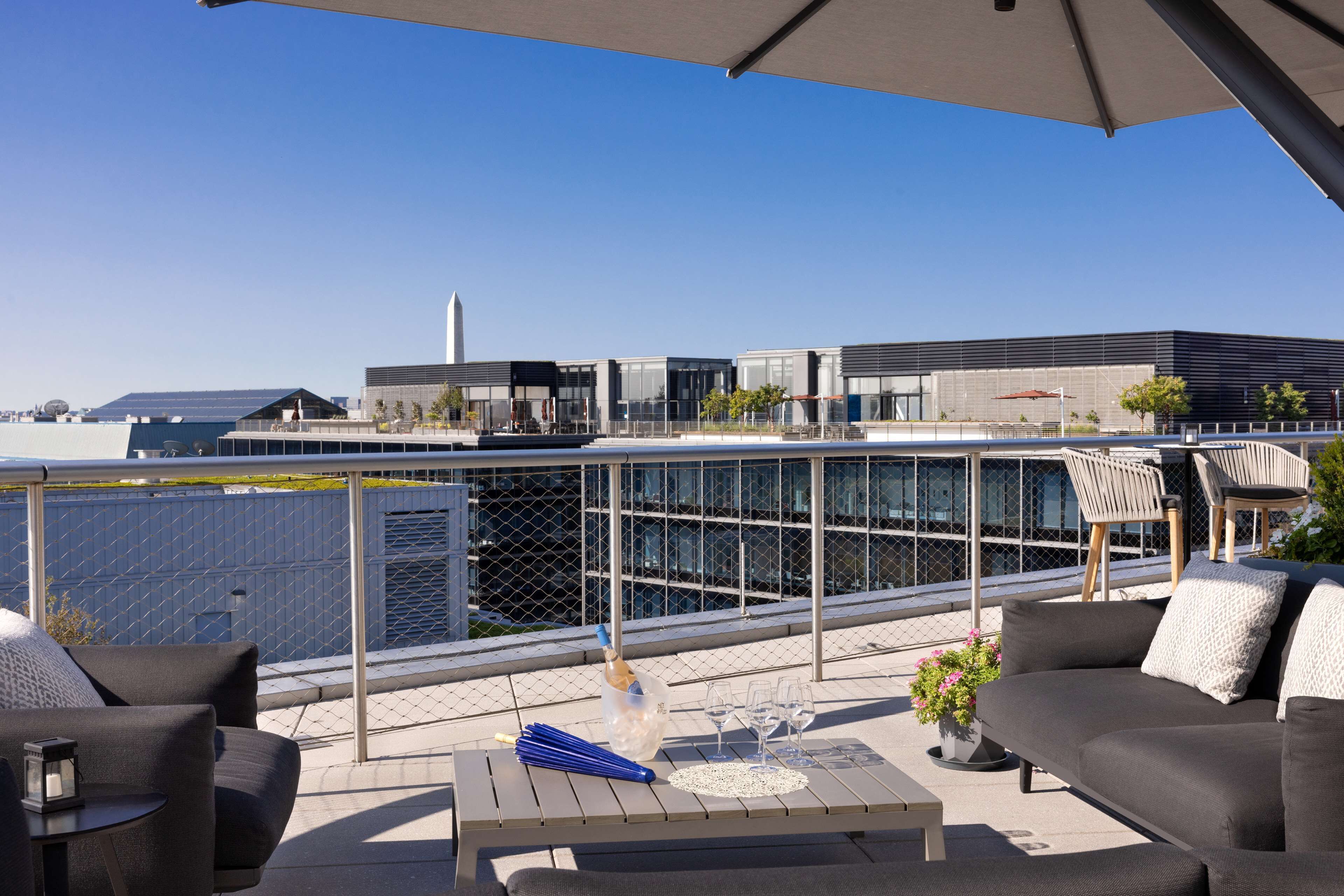 Een dakterras met buitenplaatsen, een tafel met een fles en glazen, en uitzicht op moderne gebouwen.
