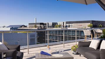 Een dakterras met buitenplaatsen, een tafel met een fles en glazen, en uitzicht op moderne gebouwen.