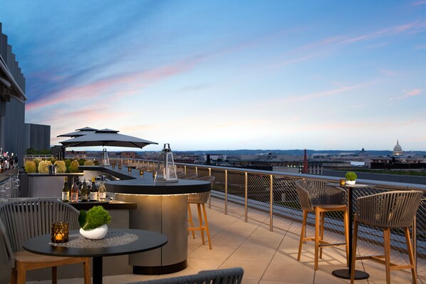 Un bar en la azotea con vistas panorámicas de la ciudad, que cuenta con una barra, zona de estar y sombrillas.