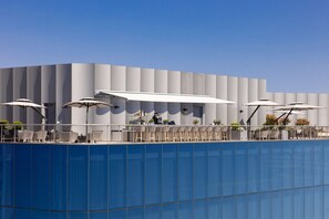 A modern building with a blue facade, outdoor seating with umbrellas, and a clear sky.