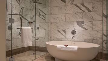 Un baño moderno con una bañera independiente, ducha con mampara de cristal y paredes con diseño de mármol.