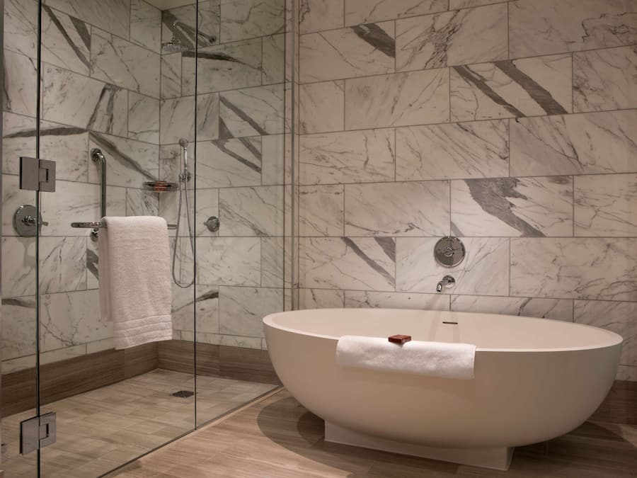 Un baño moderno con una bañera independiente, ducha con mampara de cristal y paredes con diseño de mármol.