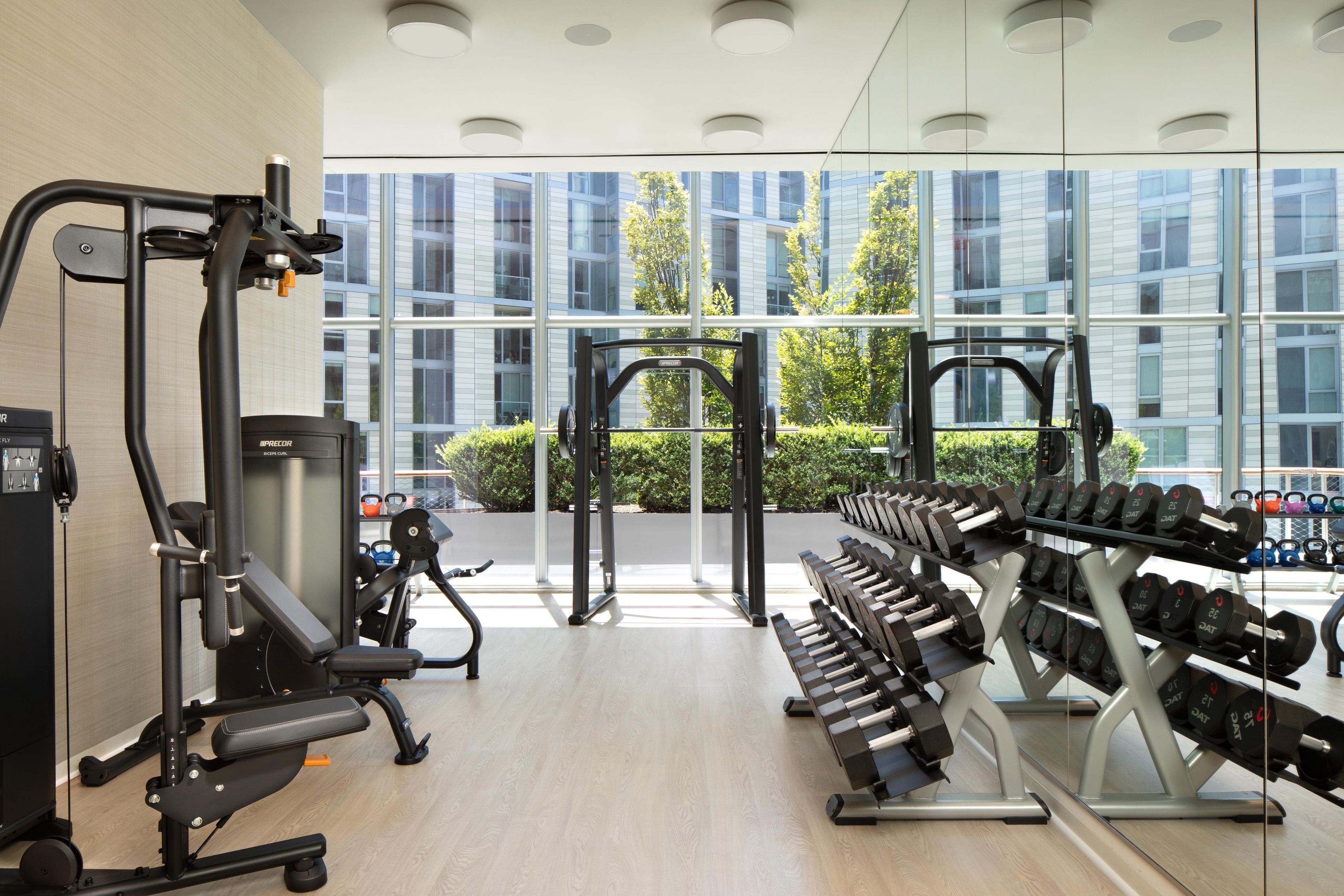 A gym with exercise equipment, weight racks, and large windows offering a view of the outside.