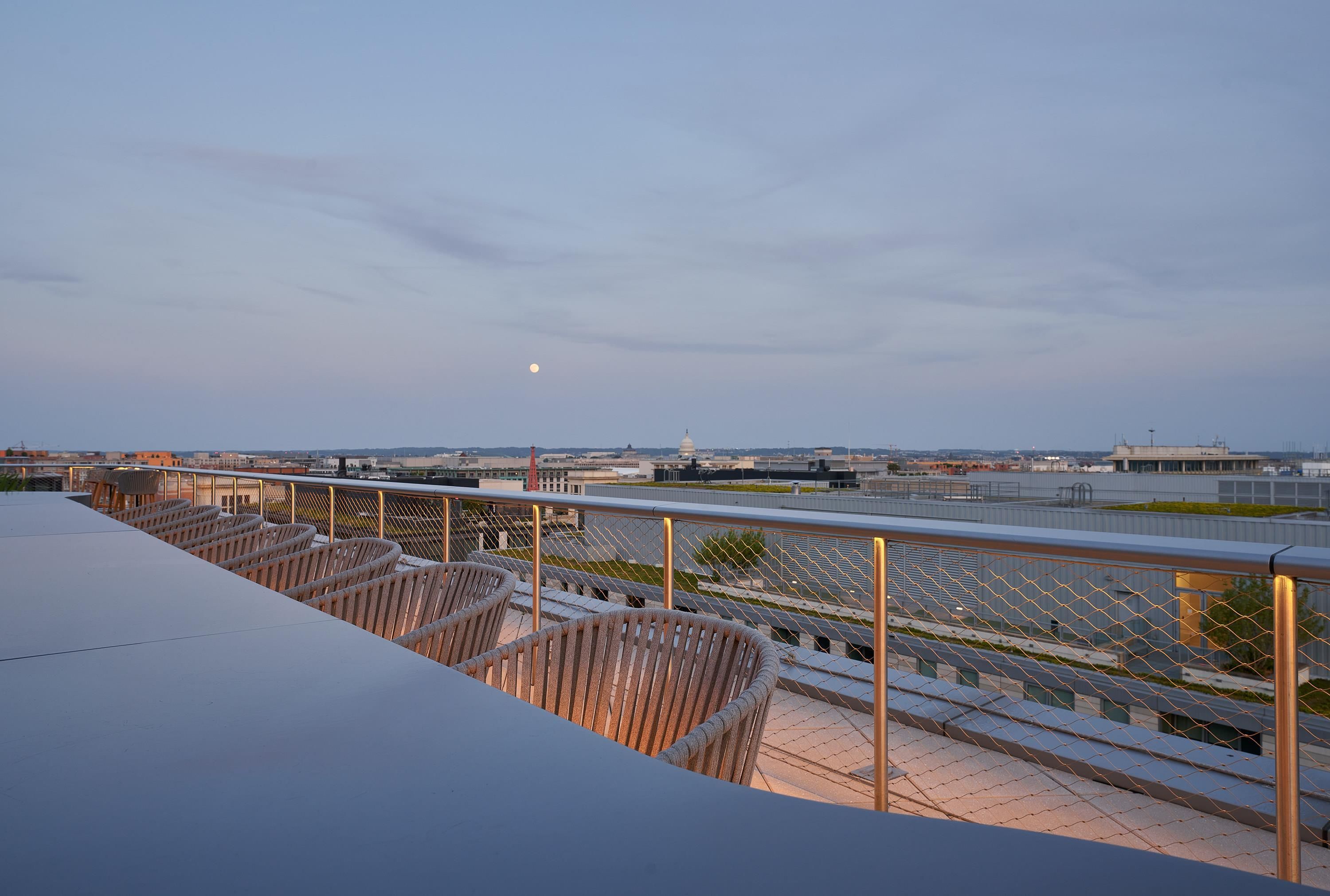 Una terraza en la azotea con barandilla de metal, sillas y vistas del paisaje urbano y un edificio distante.