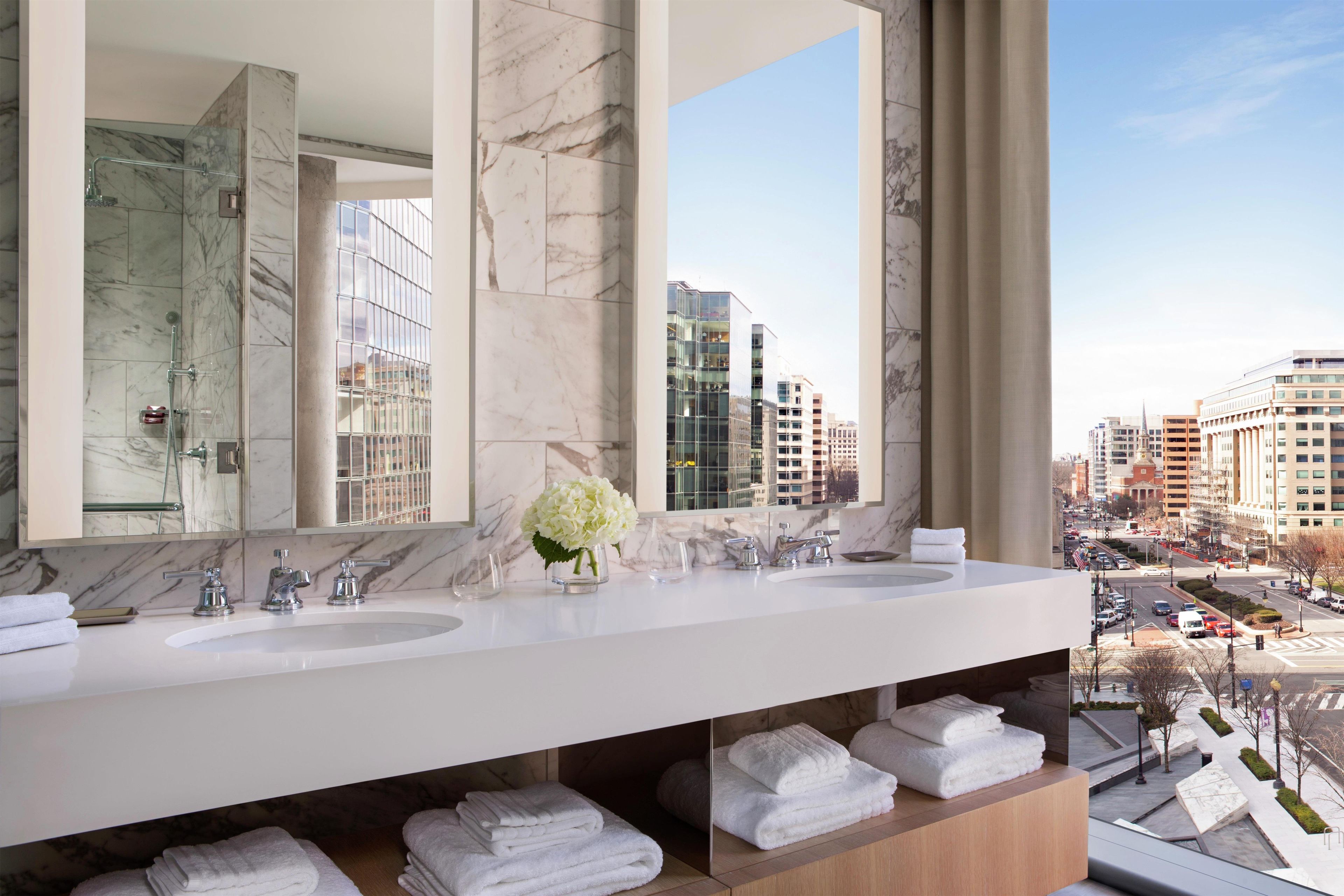 A modern bathroom with two sinks, a large mirror, and a view of the cityscape.