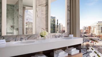 A modern bathroom with two sinks, a large mirror, and a view of the cityscape.