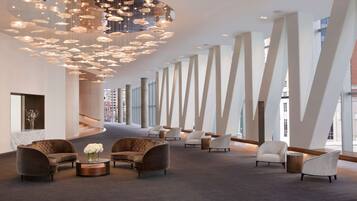 A spacious lobby with modern furniture, a unique ceiling light fixture, and large windows offering views of the city.