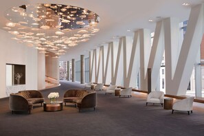 A spacious lobby with modern furniture, a unique ceiling light fixture, and large windows offering views of the city.