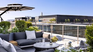A rooftop terrace with a modern outdoor seating area, including a sofa and a round table with drinks and a lantern.