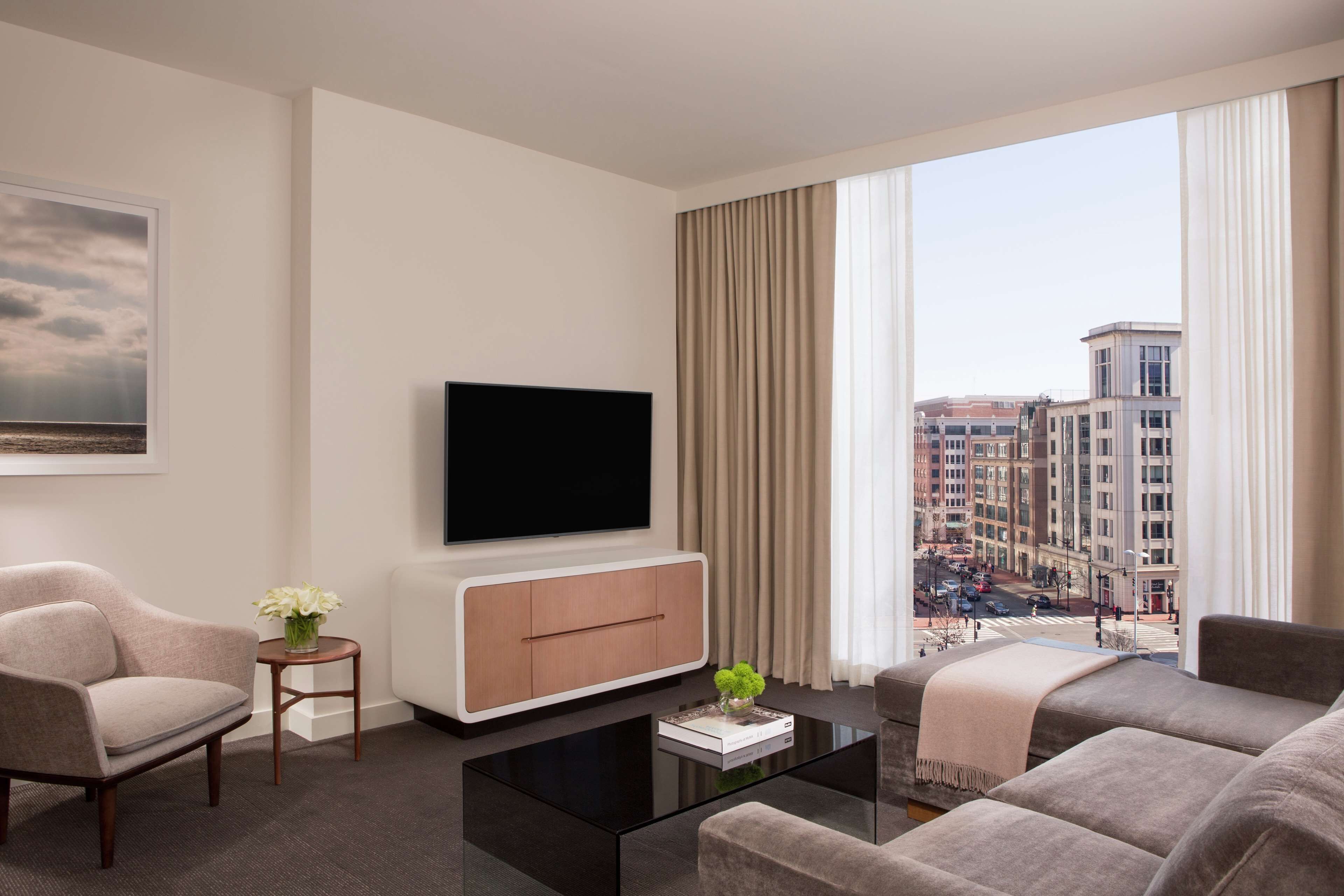 A modern living room with a flat-screen TV, a sofa, a coffee table, and a view of the city through large windows.