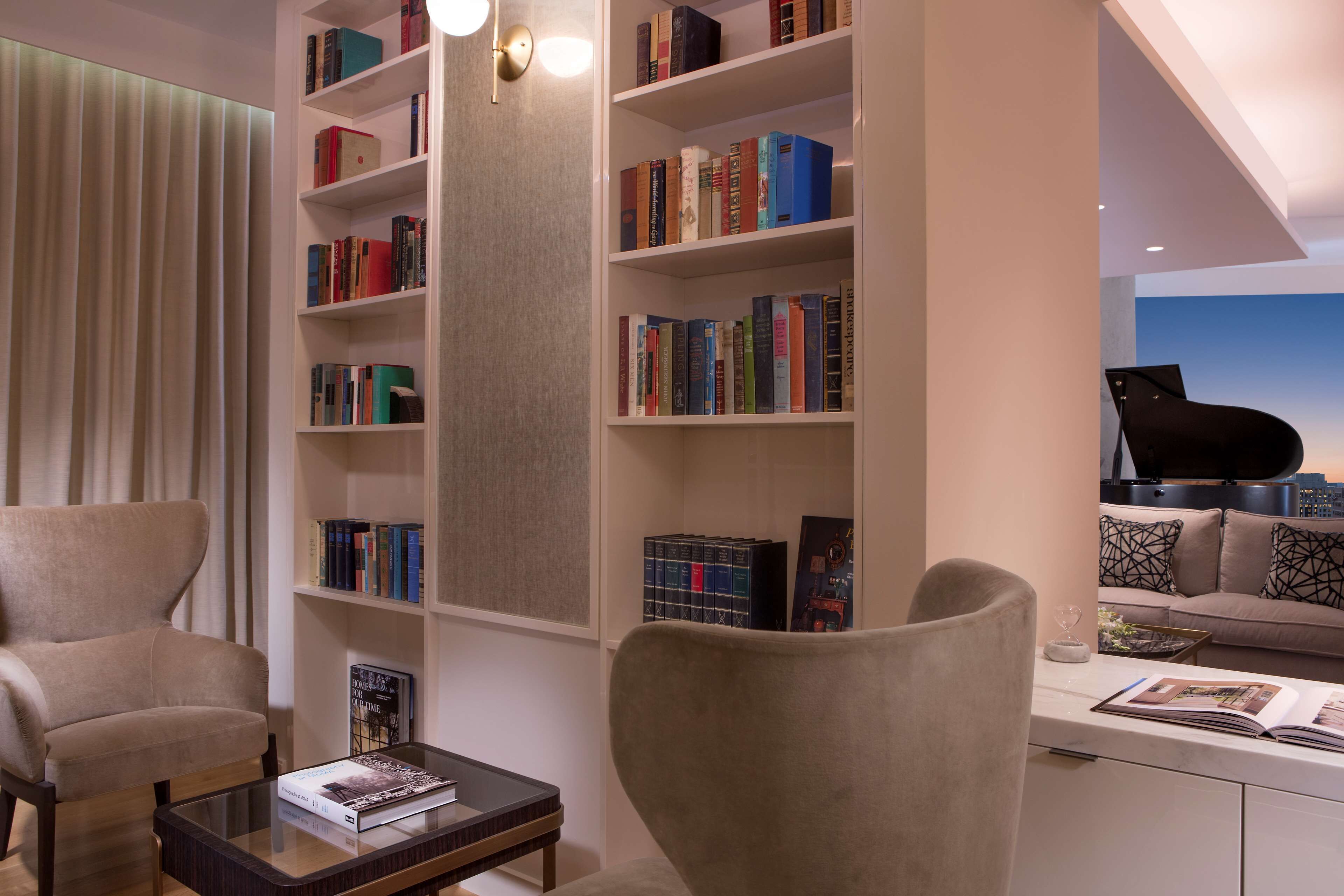 A modern living room with a large bookshelf, a piano, and comfortable seating.