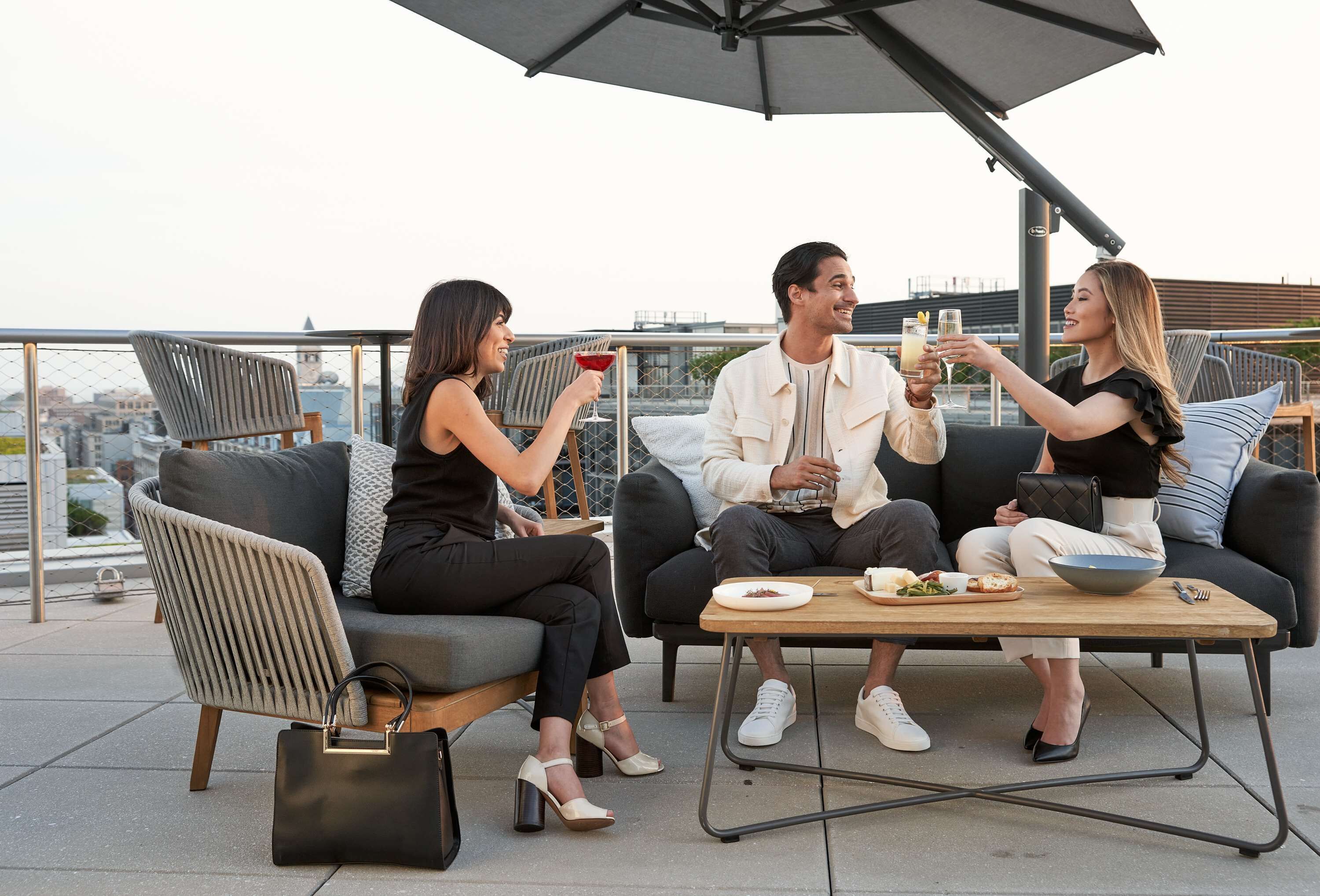 Une terrasse sur le toit avec des sièges en plein air, une table garnie de nourriture et de boissons, et une vue sur la ville en arrière-plan.