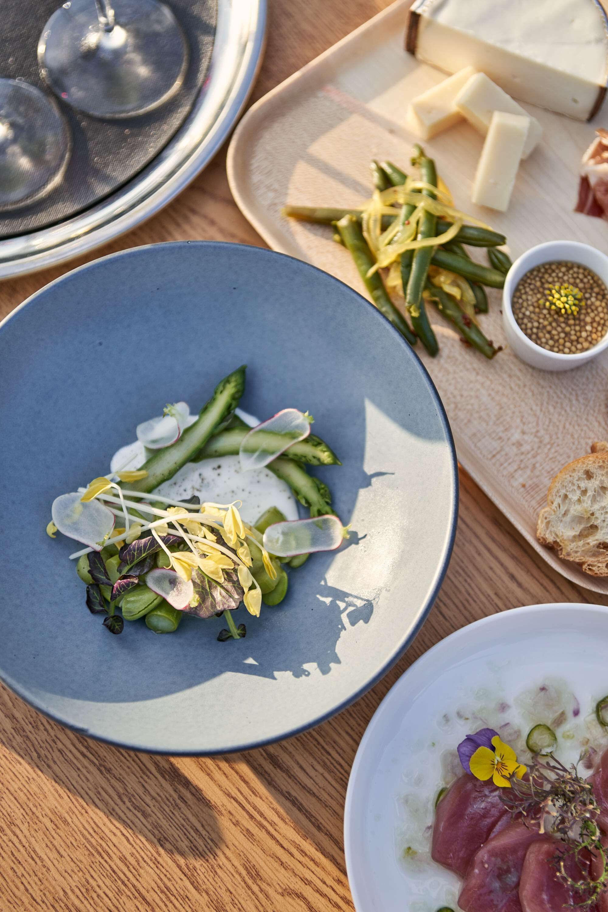 A dining table with various dishes, including a plate of green beans, cheese, and a bowl of salad.