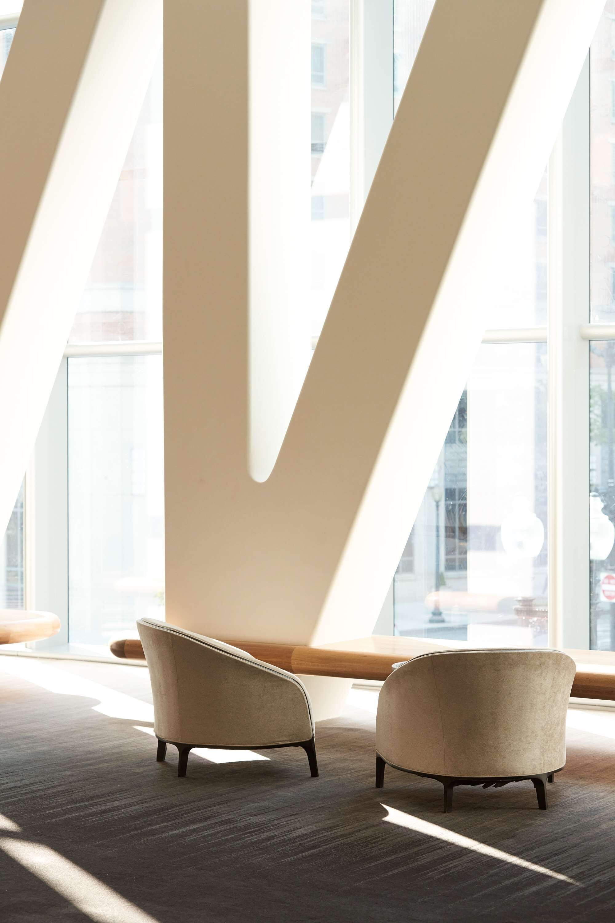 Un intérieur moderne avec deux fauteuils, un plafond haut et de grandes fenêtres qui laissent entrer la lumière naturelle.