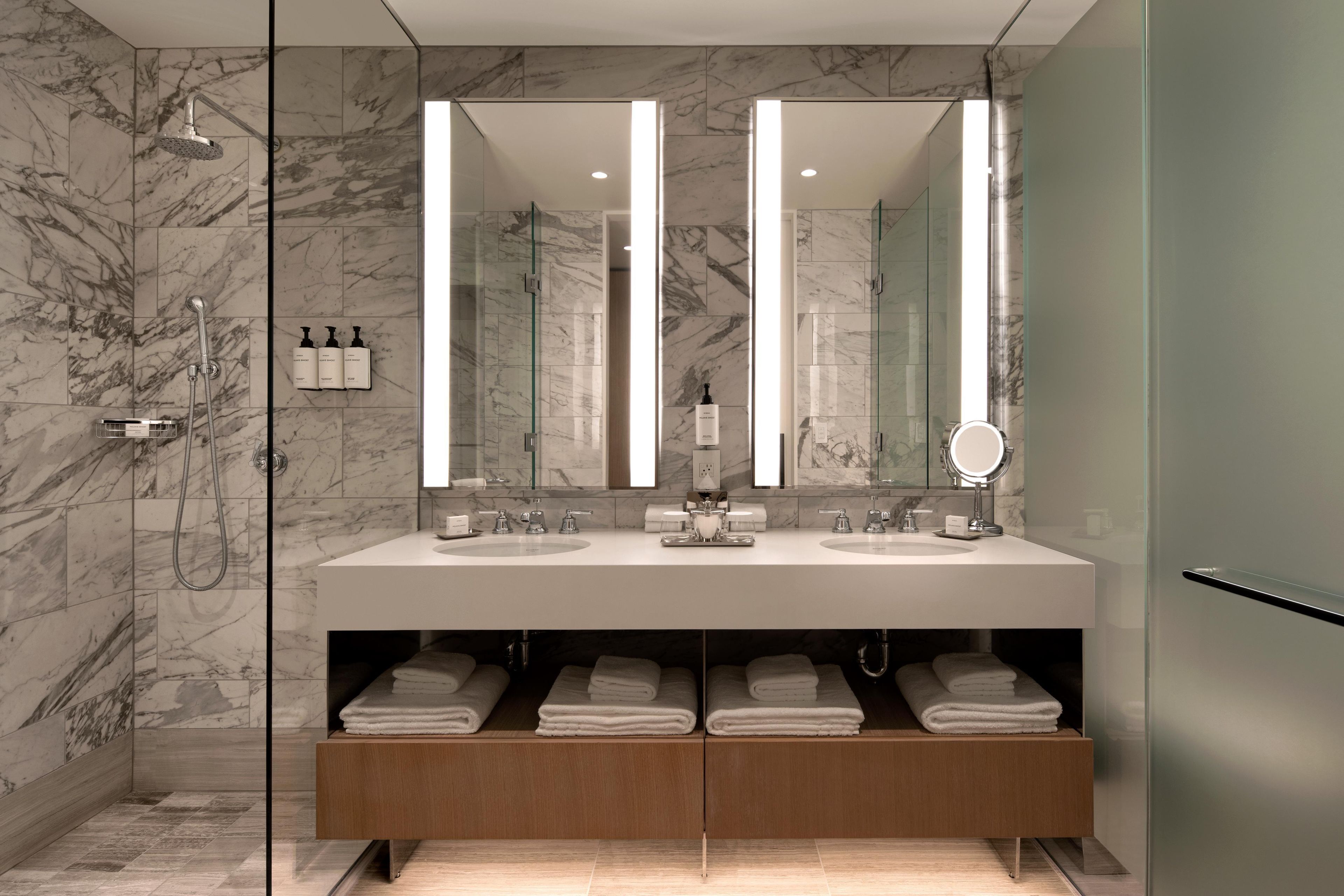 Un baño moderno con pared de mármol, tocador doble, cabina de ducha de vidrio y toallero empotrado.