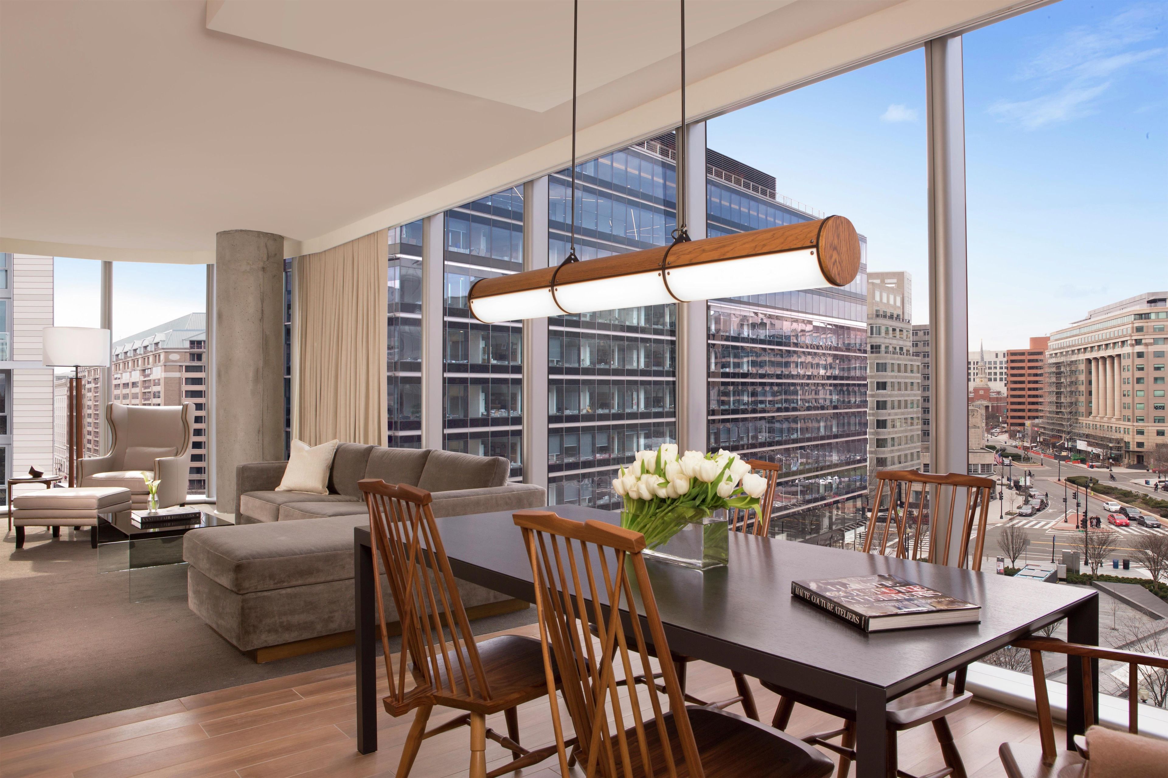 A modern living room with a dining area, large windows, and a city view.