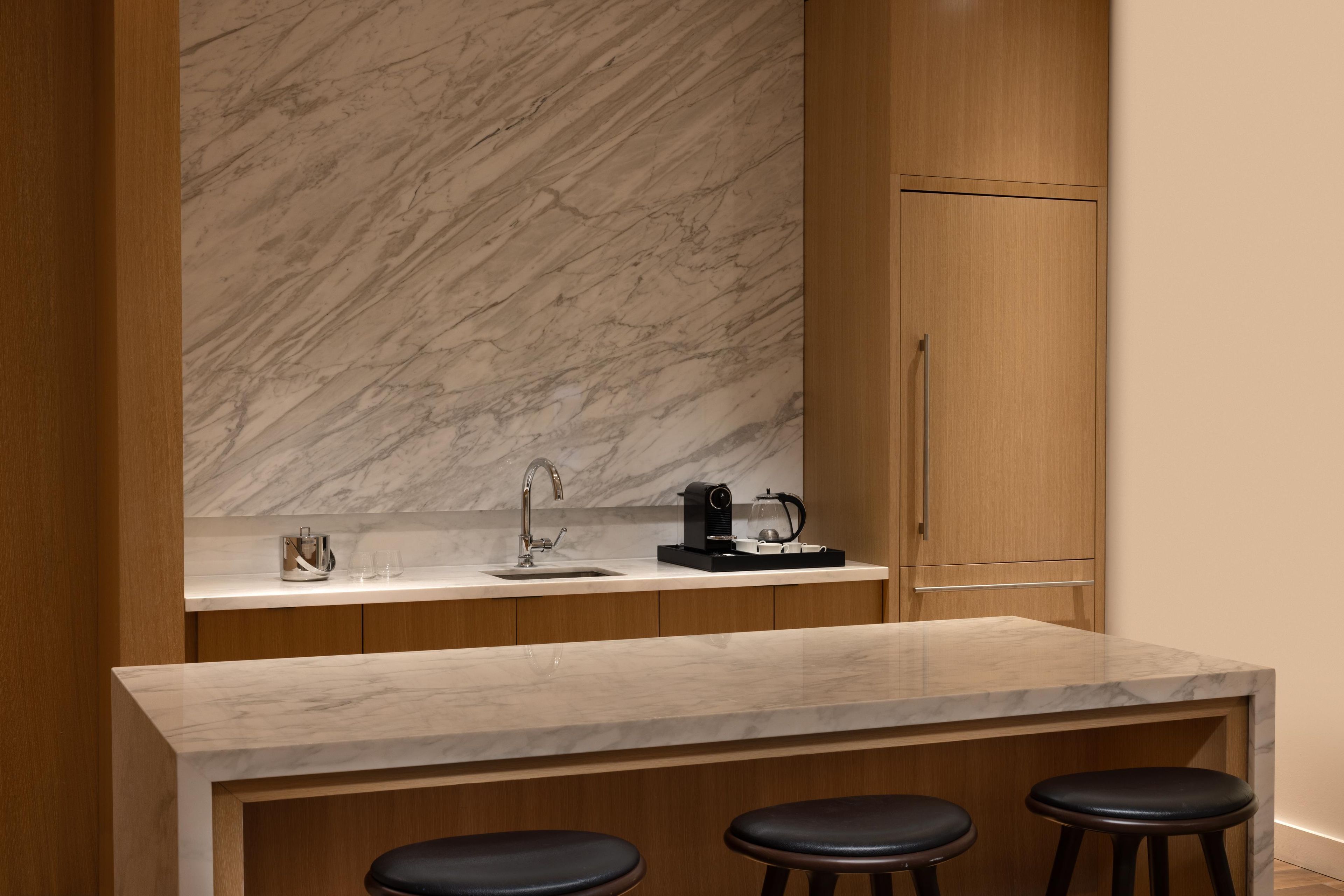 A modern kitchen with a marble backsplash, a sink, a coffee machine, and bar stools.