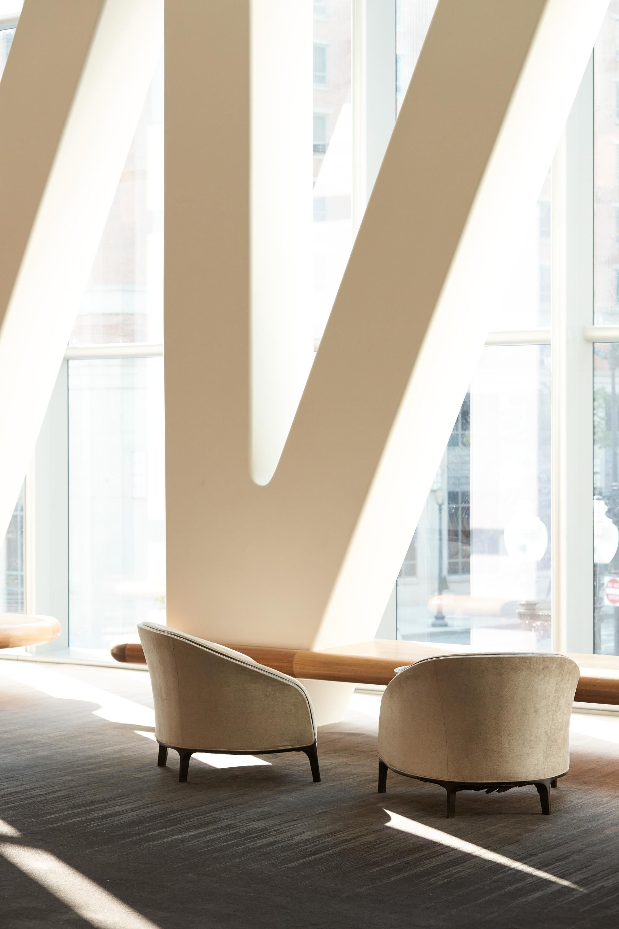 A modern interior with two armchairs, a high ceiling, and large windows.