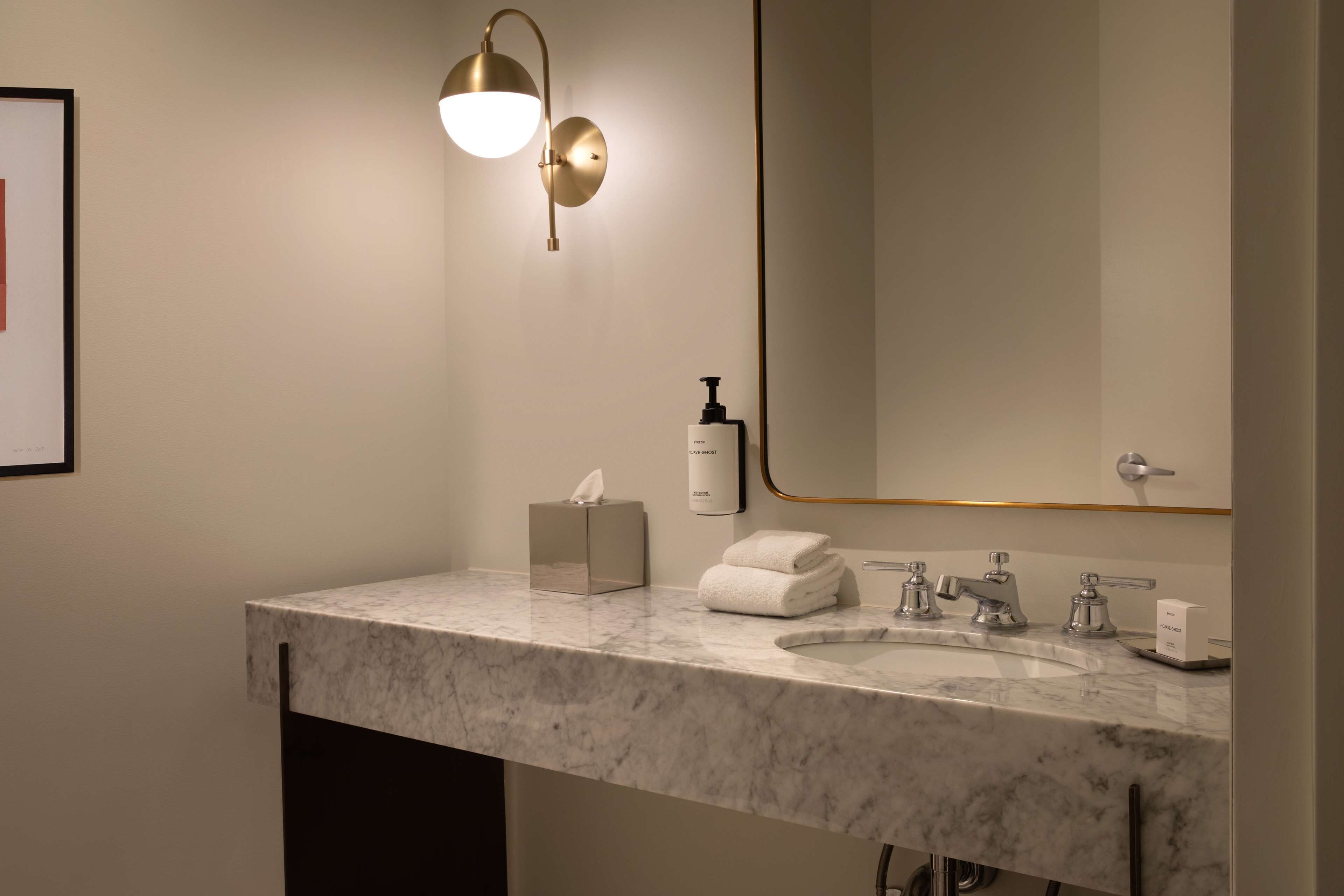 A modern bathroom with a marble sink, a large mirror, a wall-mounted light fixture, a tissue box, and a bottle of hand soap.