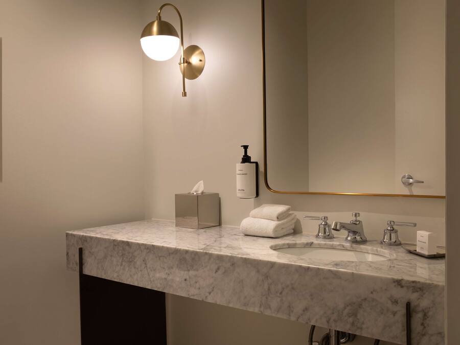 A modern bathroom with a marble sink, a large mirror, a wall-mounted light fixture, a tissue box, and a bottle of hand soap.