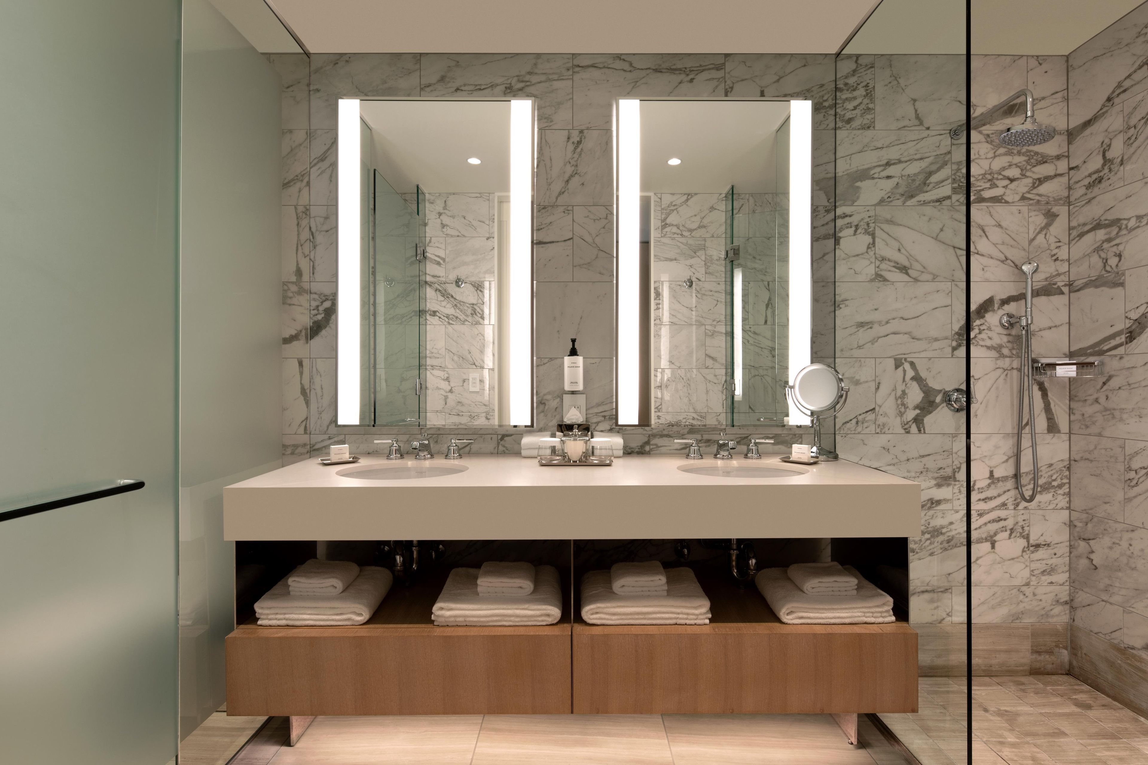 A modern bathroom with a large mirror, dual sinks, and a shower.
