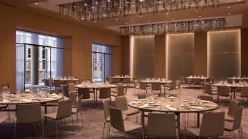 A spacious banquet hall with round tables set for dining, large windows, and a modern chandelier.