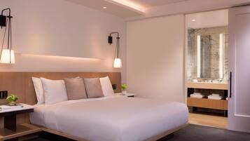 Una camera d'albergo moderna con un letto grande, comodini, un tavolino, un lampadario a parete, un bagno con doccia in marmo e un mobile bagno integrato.