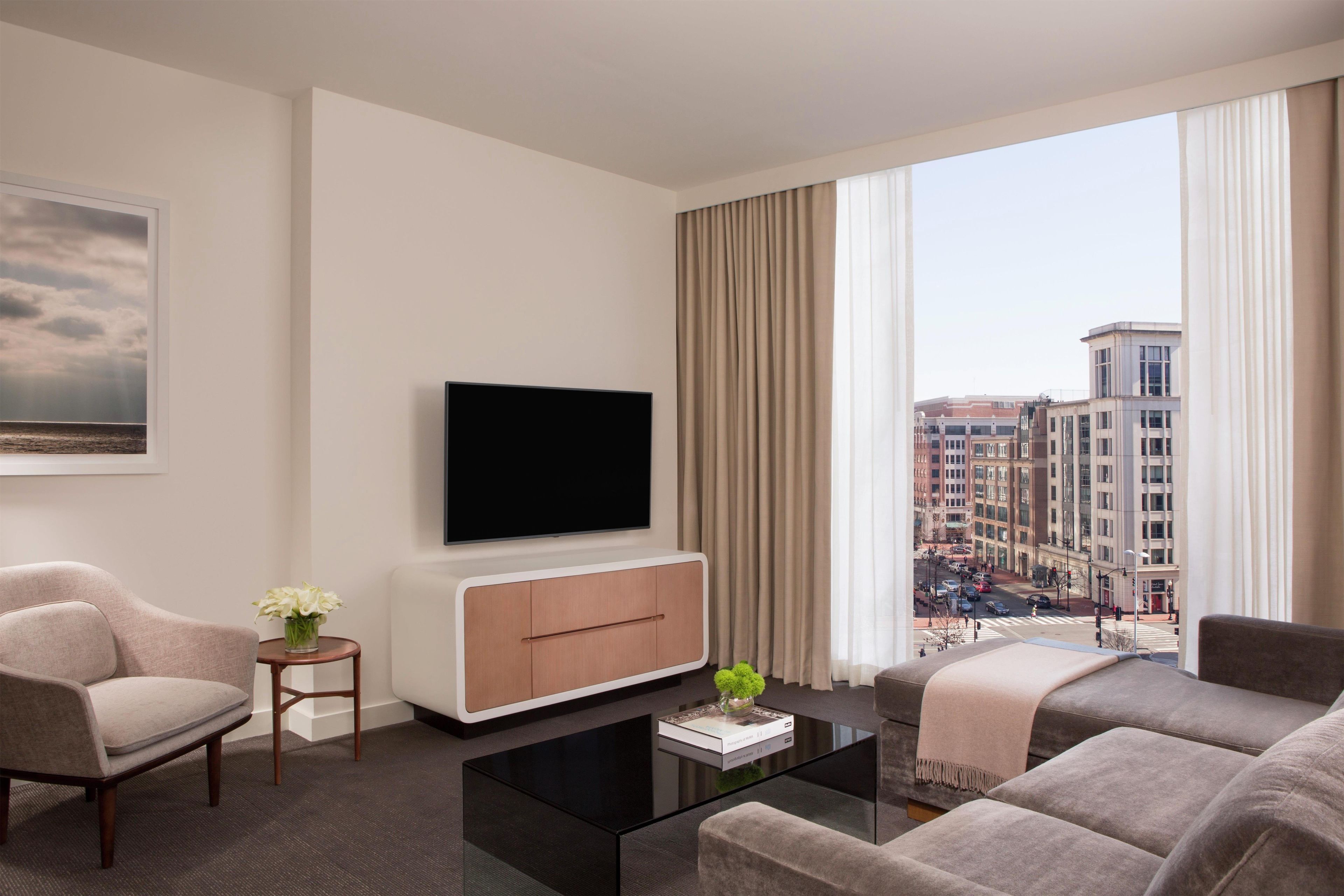 Habitación de hotel moderna con televisor de pantalla plana, sofá, mesa de centro y vista panorámica de la ciudad.