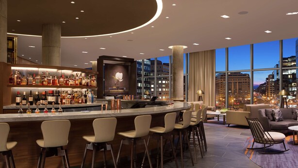 A modern bar area with a variety of liquor bottles, a large circular bar counter, and a seating area with sofas and chairs.