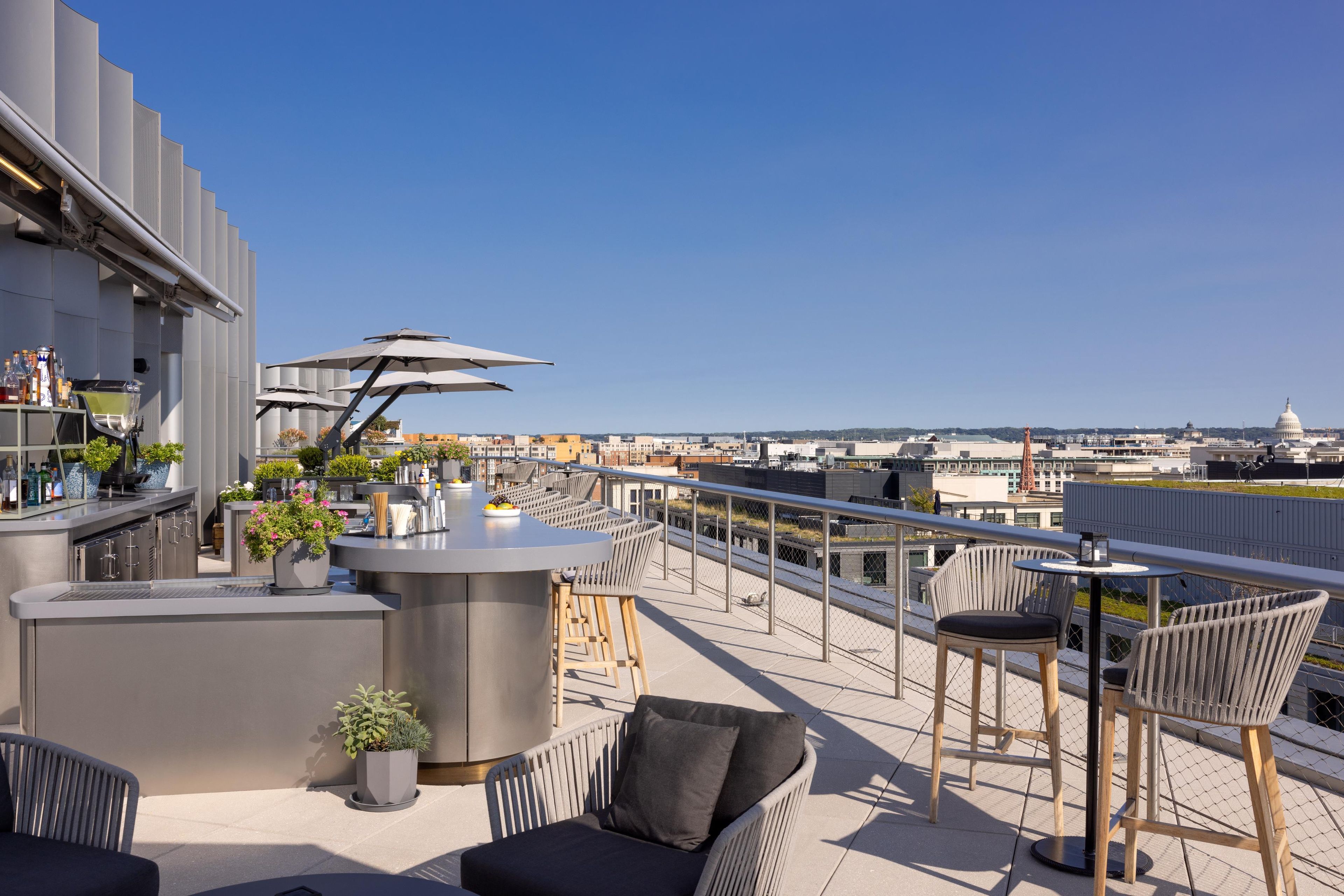 Eine Dachterrasse mit Barbereich, Außenmöbeln und Blick auf die Stadtlandschaft, darunter eine markante Kuppel.