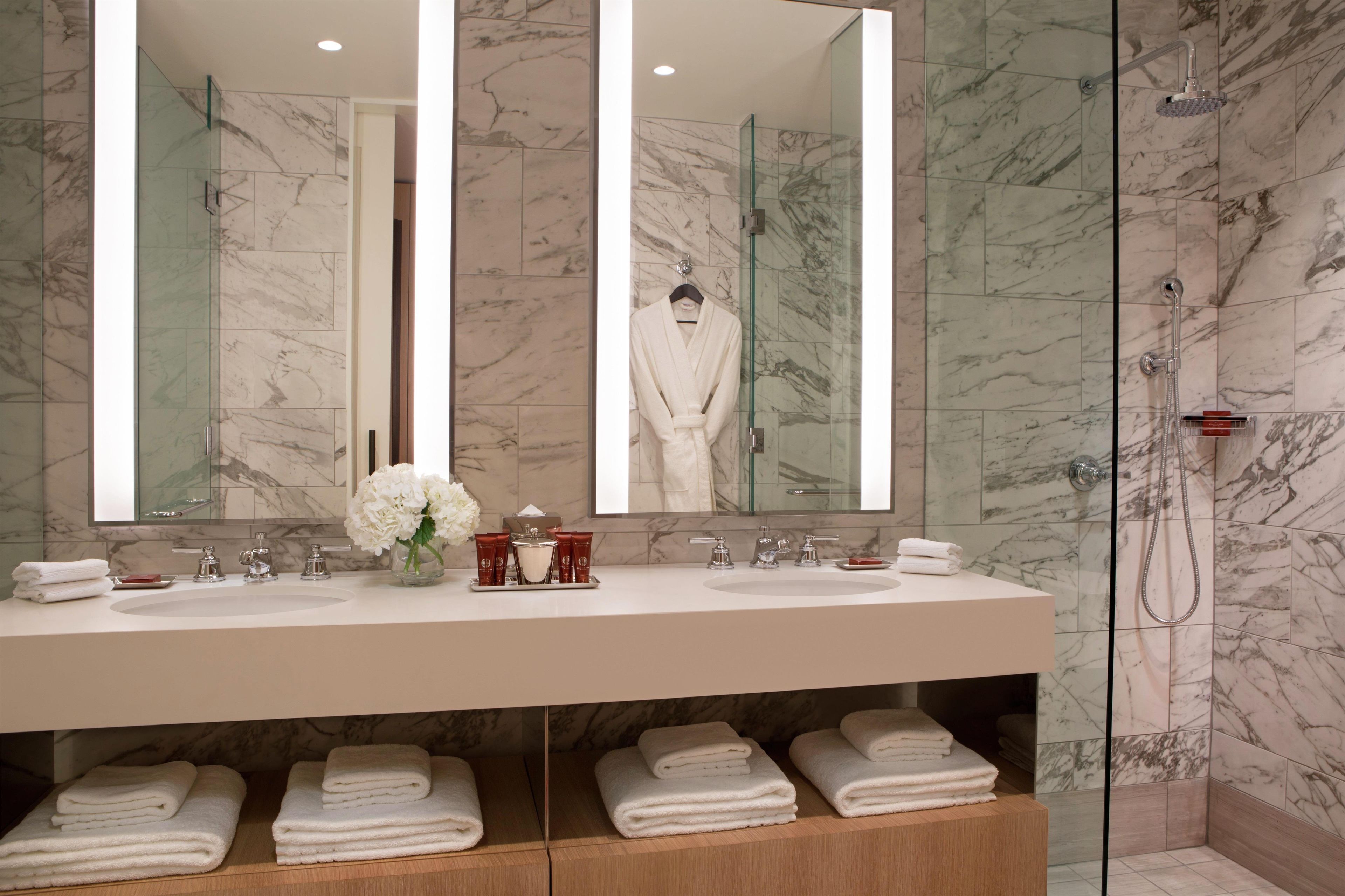 Une salle de bain dotée d’un grand miroir, de deux lavabos, d’une douche en verre et de serviettes soigneusement pliées.