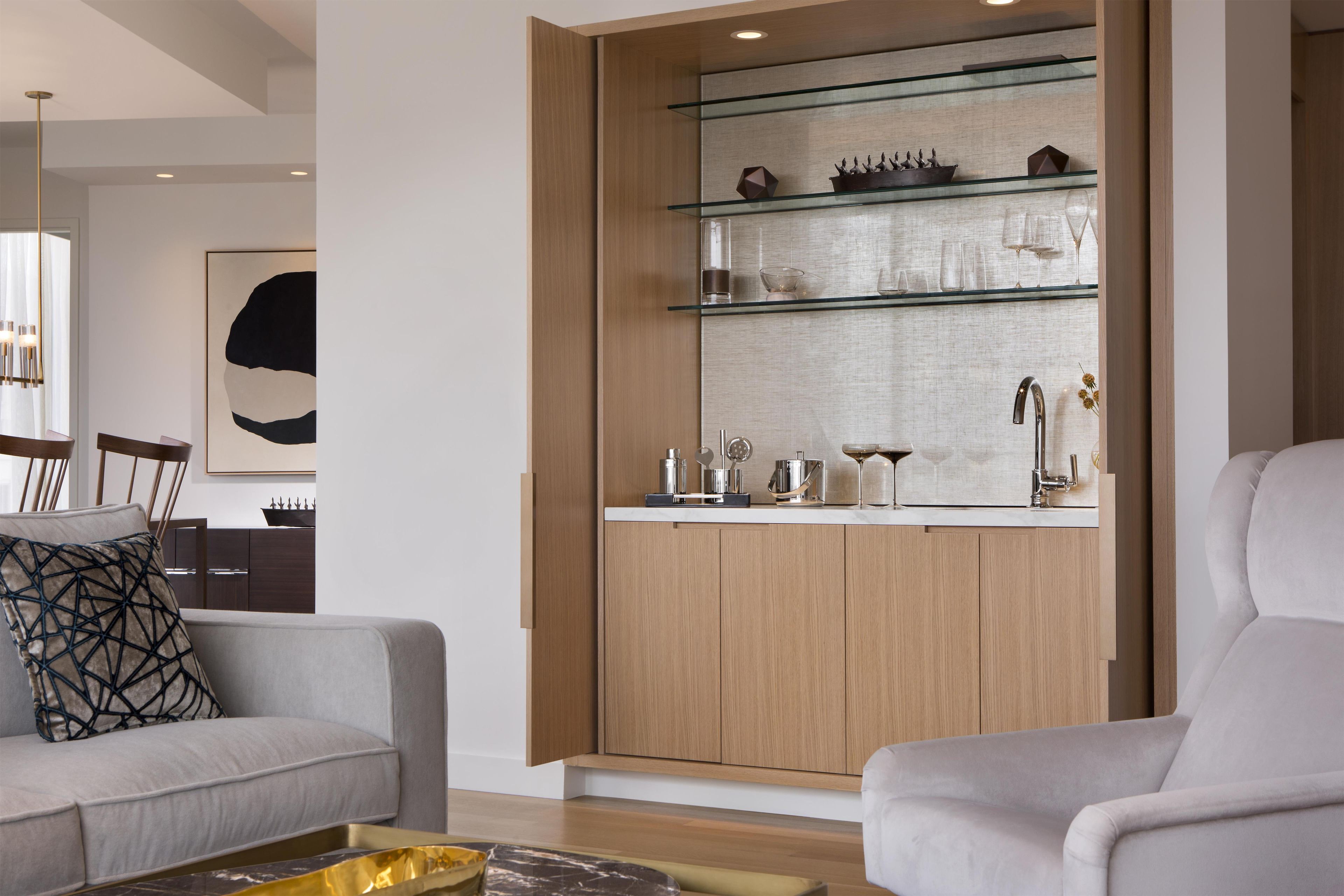 A modern living room with a built-in kitchen area featuring a glass shelf display and a marble coffee table.