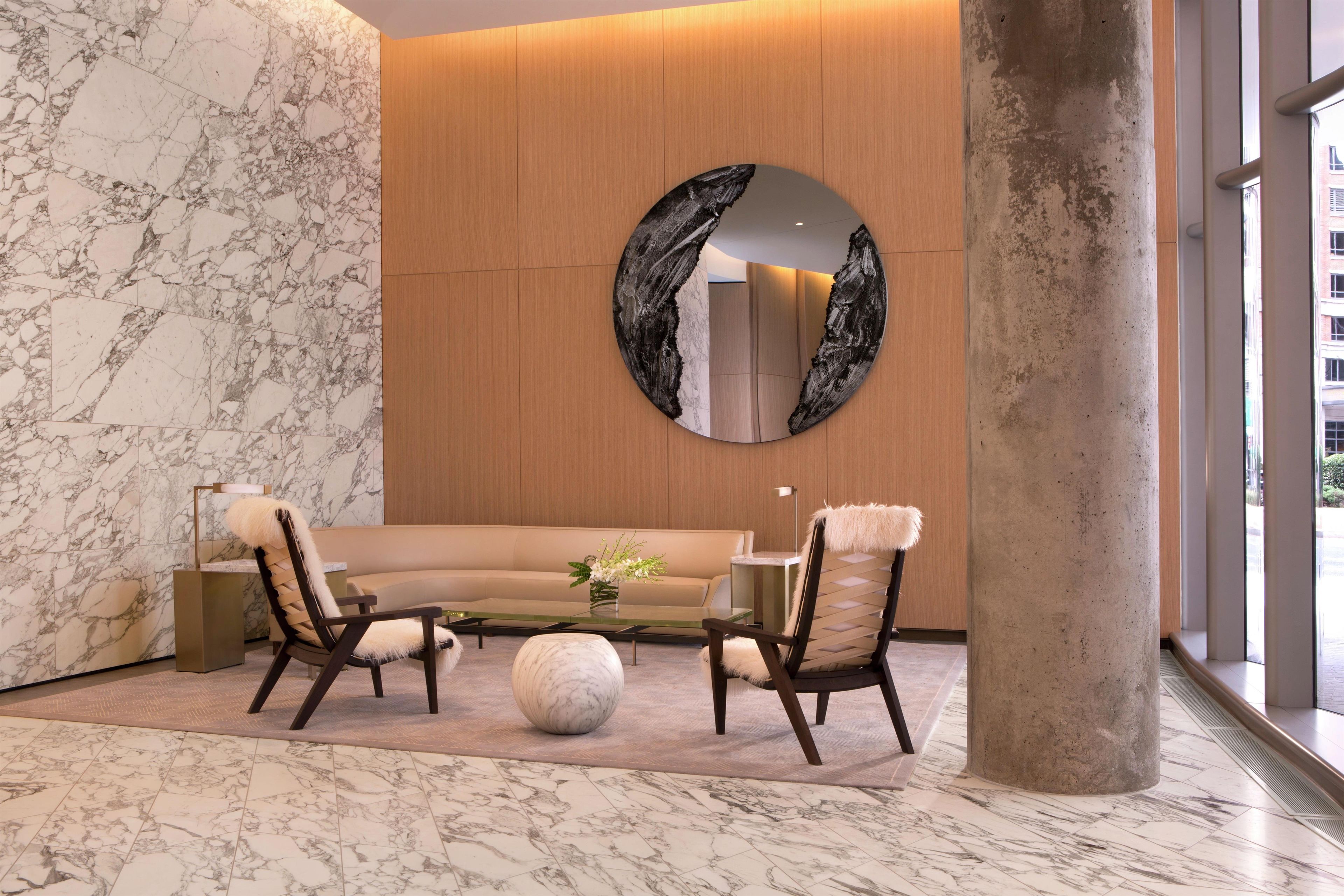 Un interior moderno con una pared de mármol, un espejo redondo, un sofá, dos sillones, una mesa de centro y una columna grande.