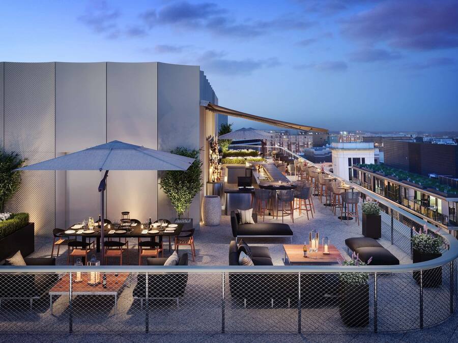 Un área de comedor al aire libre con mesas, sillas, sombrillas y vistas de la ciudad.