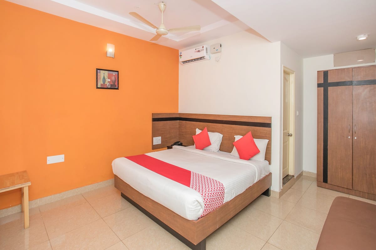 A hotel room with a bed, a ceiling fan, an air conditioning unit, and a wardrobe.