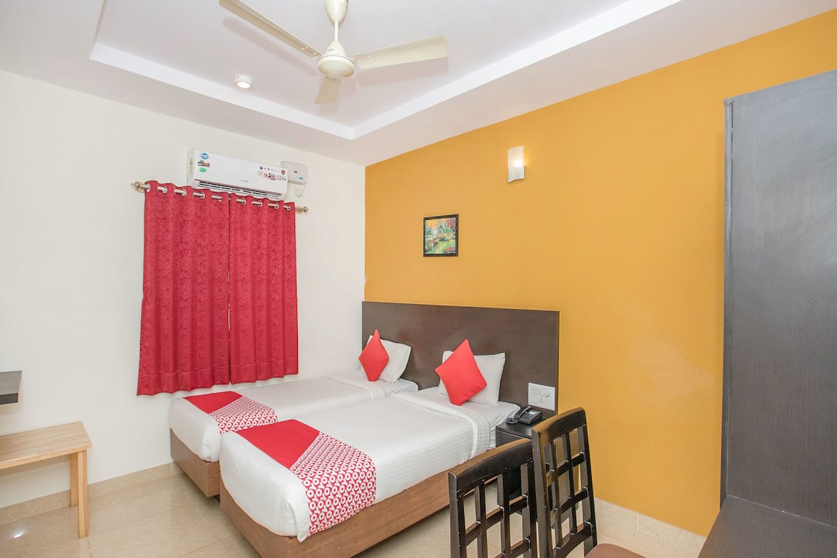 A hotel room with a bed, a desk, a chair, a ceiling fan, and a wall-mounted air conditioner.