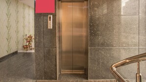 An elevator in a lobby with a red sign above it and a decorative item on the wall. - OYO 7846 Hotel The Prince Gardenia (Bengaluru)