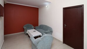 Quarto pequeno com parede vermelha, porta de madeira e dois poltronas cinzentas com uma mesinha.