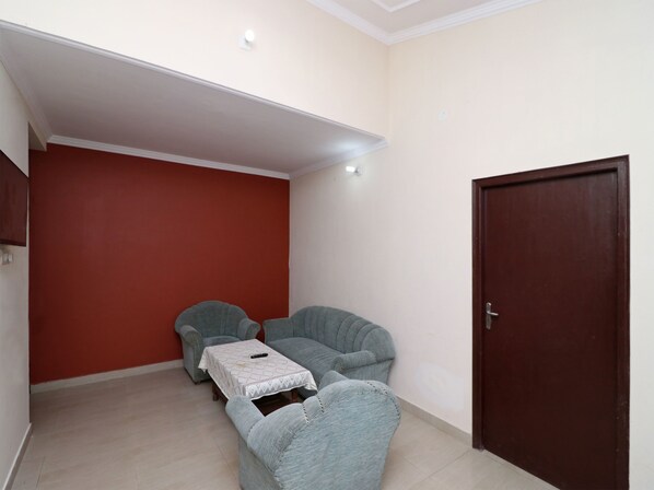 Una habitación pequeña con una pared roja, una puerta de madera y dos sillones grises con una mesita.