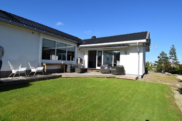 A modern house with a covered patio, a lawn, and outdoor furniture. - Solferie Holiday Home Tornestien (Kristiansand)