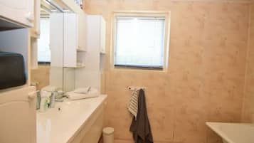 A bathroom with a white sink, mirror, and window. There is a towel rack with a towel and a trash can.