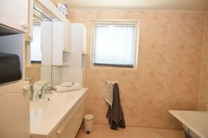A bathroom with a white sink, mirror, and window. There is a towel rack with a towel and a trash can. - Solferie Holiday Home Tornestien (Kristiansand)