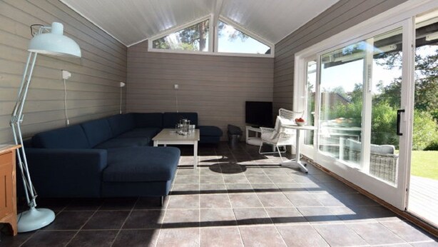 Una habitación iluminada por el sol, con un sofá seccional azul oscuro, una mesita, un televisor y un ventanal de vidrio que da al exterior.