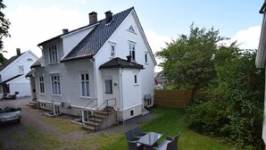 A white two-story house with a tiled roof, a front porch with steps, and a small outdoor seating area with a table and chairs. - Solferie Holiday Apartment Østerveien (Kristiansand)