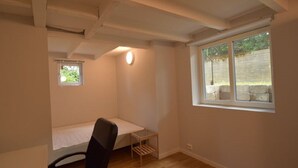 A small, single-room apartment with a bed, a desk, a chair, a small window, and a light fixture. - Solferie Holiday Apartment Østerveien (Kristiansand)
