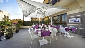 Un espace de restauration en plein air avec des tables et des chaises, un grand parasol et une enseigne indiquant « Le Camere del Crimine ».
