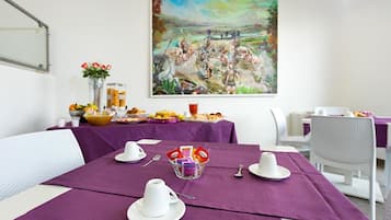 A dining area with a table set for breakfast, including cups, a bowl of fruit, and a painting on the wall.