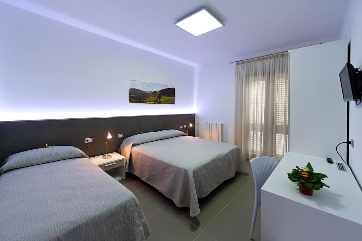 A hotel room with two beds, a desk, a TV, and a window with curtains.